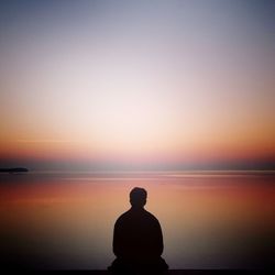 Rear view of silhouette man standing at beach against sky during sunset