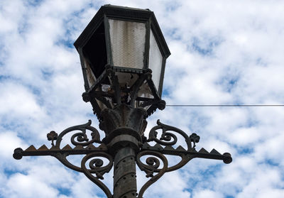 Low angle view of broken street lamp against cloudy sky