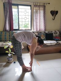 Side view full length of woman exercising in living room at home