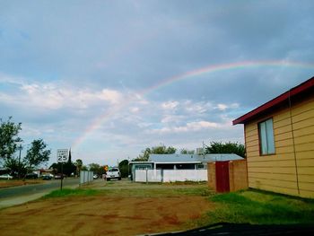 Rainbow over building and houses against sky