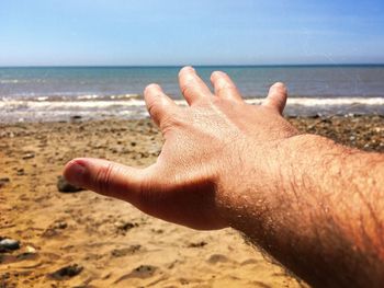 Close-up of hand on sand at beach against sky