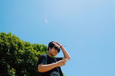 Low angle view of man using phone against clear blue sky