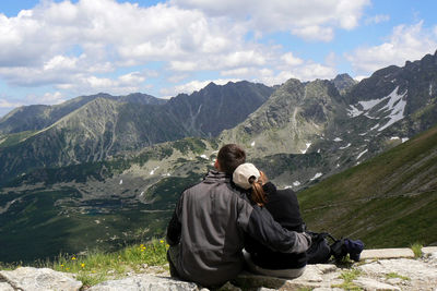 Man sitting on mountain against sky