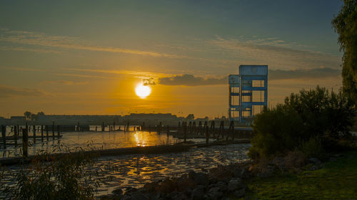 Scenic view of river by buildings against sky during sunset