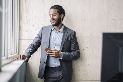 Young businessman standing at window, holding smart phone