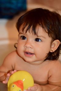 Close-up of cute baby girl playing with rubber duck while bathing in bathtub