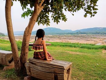 Man sitting on land by trees against sky