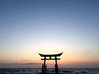 Silhouette lifeguard hut on sea against sky during sunset