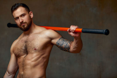Portrait of muscular man with katana sword against wall