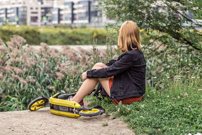 Young woman sitting in the green grass in the park. relaxing with scooter 