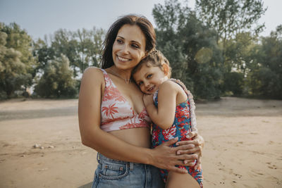 Mother and daughter embracing while standing at beach
