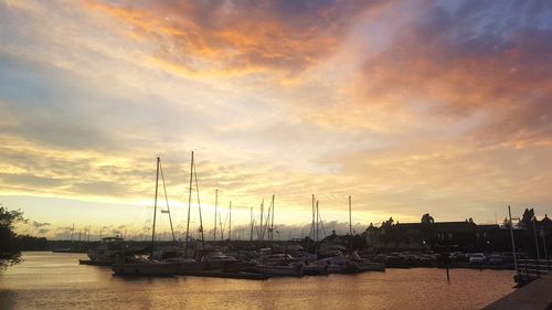 Sailboats moored at harbor against sky during sunset