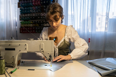 Young design studio owner female at workplace sew clothes on sewing machine in professional atelier
