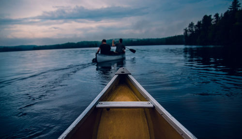 Male friends sailing boat in lake against sky