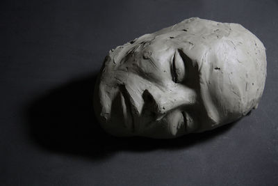 Clay sculpture, with closed eyes. face with shadows, lying on black floor