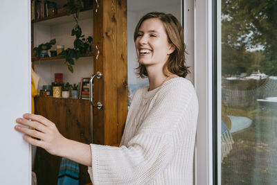 Happy young woman wearing sweater while standing at doorway