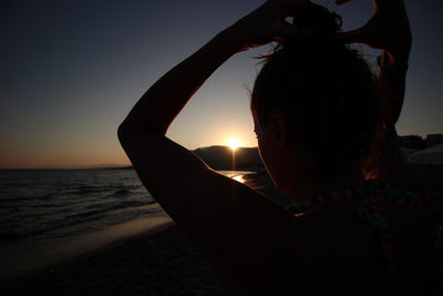 Rear view of silhouette woman standing at beach during sunset