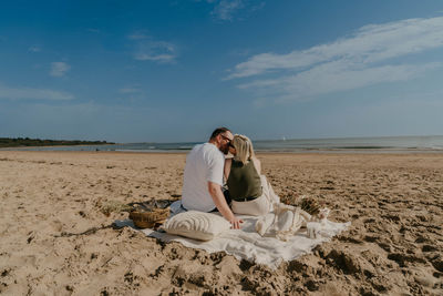 Rear view of woman sitting on beach against sky