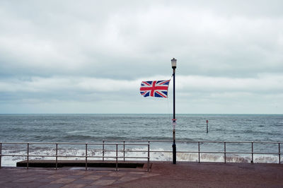 British flag on sidewalk by sea against cloudy sky