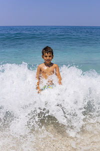 Portrait of boy splashing water in sea against sky