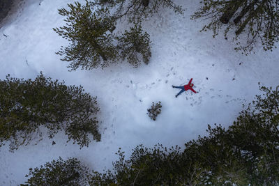 Drone aerial of woman wearing warm clothing lie down at fresh snow in winter