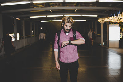 Young man looking at wristwatch while standing on footbridge at night