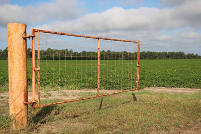 Fence on grassy field against cloudy sky