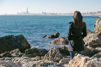 Woman standing between rocks looking at the sea on a sunny winter day