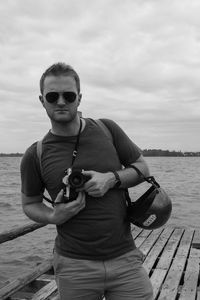 Portrait of young man holding sunglasses against sea