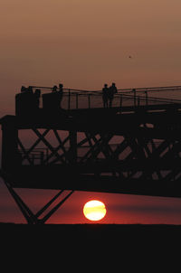 Silhouette people standing by sea against sky during sunset