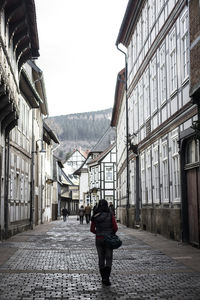 Full length rear view of woman walking on alley amidst buildings in town