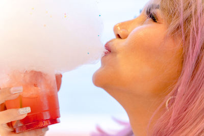 Close-up of woman eating cotton candy over drink 
