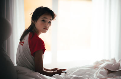 Portrait of girl sitting on bed at home