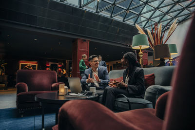 Smiling male professional discussing with female colleague sitting in hotel lounge