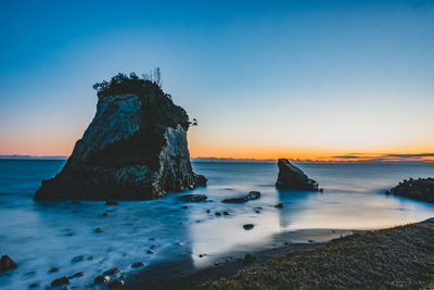 Rock formation on beach against sky during sunset