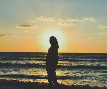 Silhouette woman standing on beach against sky during sunset