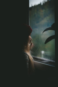 Side view of woman looking through window in rainy season