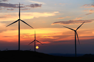 Windmills on silhouette landscape against romantic sky at sunset