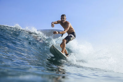 Man balancing while surfing in sea against clear sky