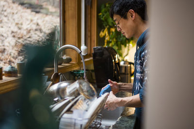 Side view of a man washing dishes in the kitchen in front of a window