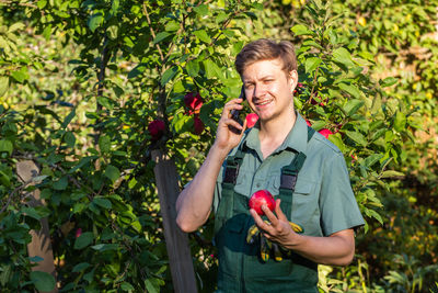 Portrait of young man holding fruit while standing against plants