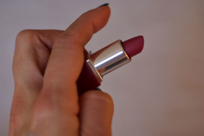 Cropped hand of woman holding lipstick against wall