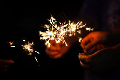 Cropped image of people holding sparklers against black background