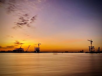 Cranes at commercial dock against sky during sunset