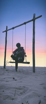 Men sitting on swing against clear sky during sunset