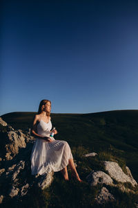 Woman sitting on rock against clear sky