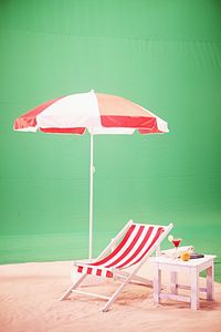 Empty deck chair with parasol on sand against green wall