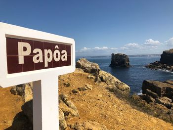 Information sign on rock by sea against sky