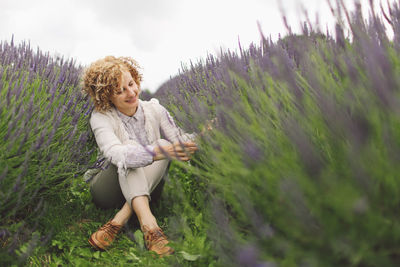 Woman looking at lavender flowers while sitting on field