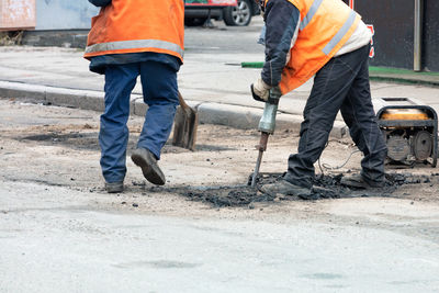 The work crew breaks up the old asphalt with an electric jackhammer on repaired section of the road.